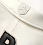 White aviator leather bomber jacket men with collar, zip closure, patch design, side pockets, and bold back logo detail.