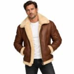 Brown shearling leather jacket with a plush cream collar, full lining, zip closure, angled pockets, buckle details, ribbed sleeves and soft trim on a white background.