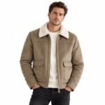 Man wearing the HAVOC brown leather shearling jacket with a cream shearling collar, front zipper, stitched panels, and practical flap pockets against a white background.